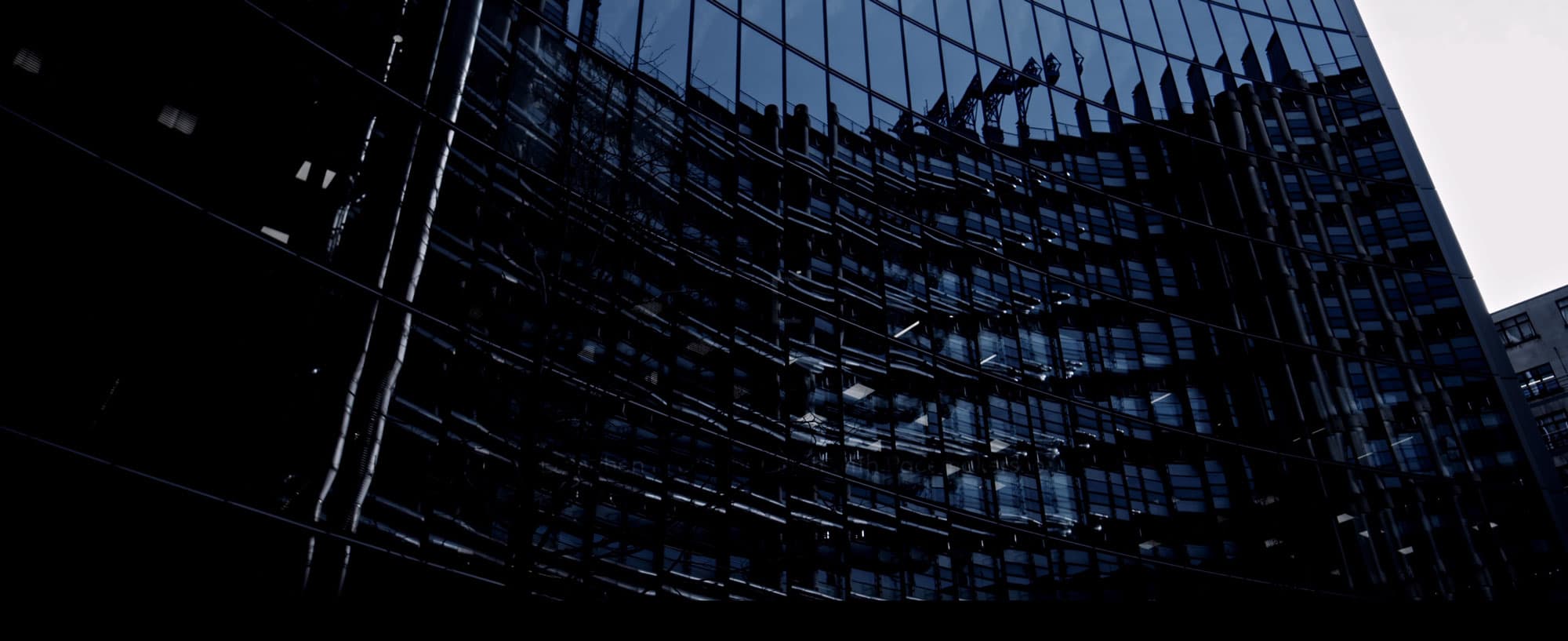Dark glass building with the reflection of another structure, creating dynamic patterns of light and shadow.