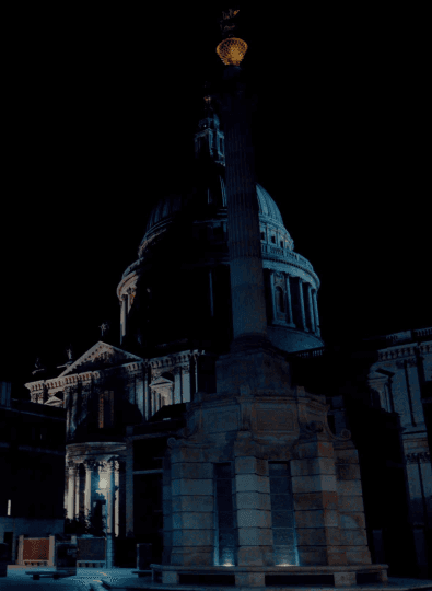 Domed building and tall column with a golden finial at night, with a bright moon in the dark sky