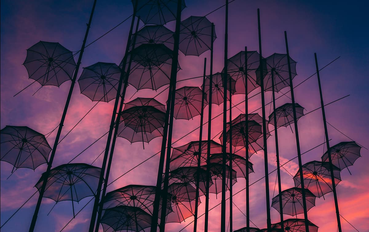 Silhouetted umbrellas hanging on poles against a purple and pink sunset sky