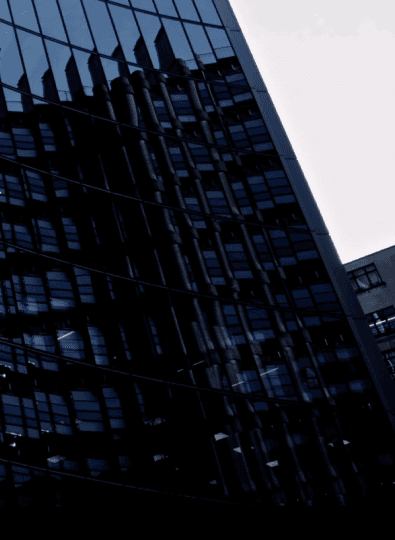 Dark glass office tower with building reflections against a pale sky
