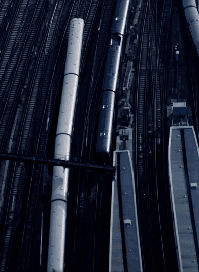 Aerial view of train tracks, long train carriages and station platform roofs in cool blue tones