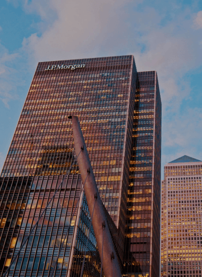 Tall glass office towers with lit windows, one with a "J.P.Morgan" sign, seen from below against a blue sky