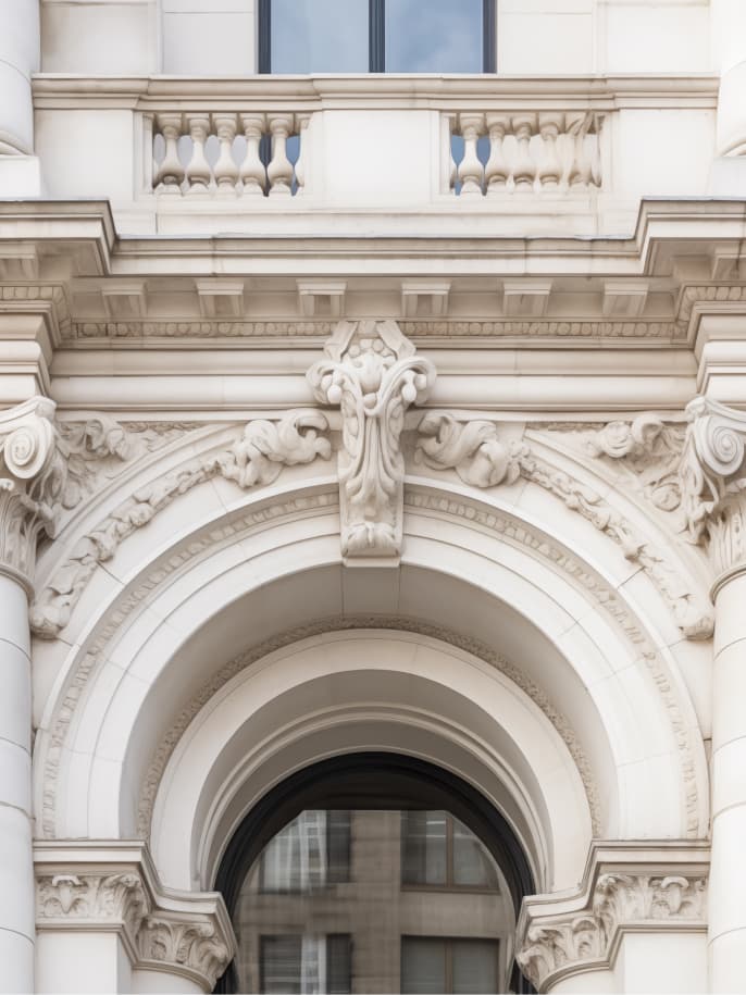 Close-up of an ornate cream stone building facade with a carved arch, balustrade and decorative keystone