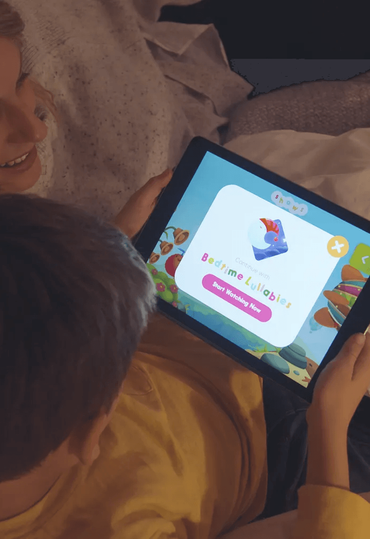 Two children lying down watching the Hopster 'Bedtime Lullabies' screen on a tablet.