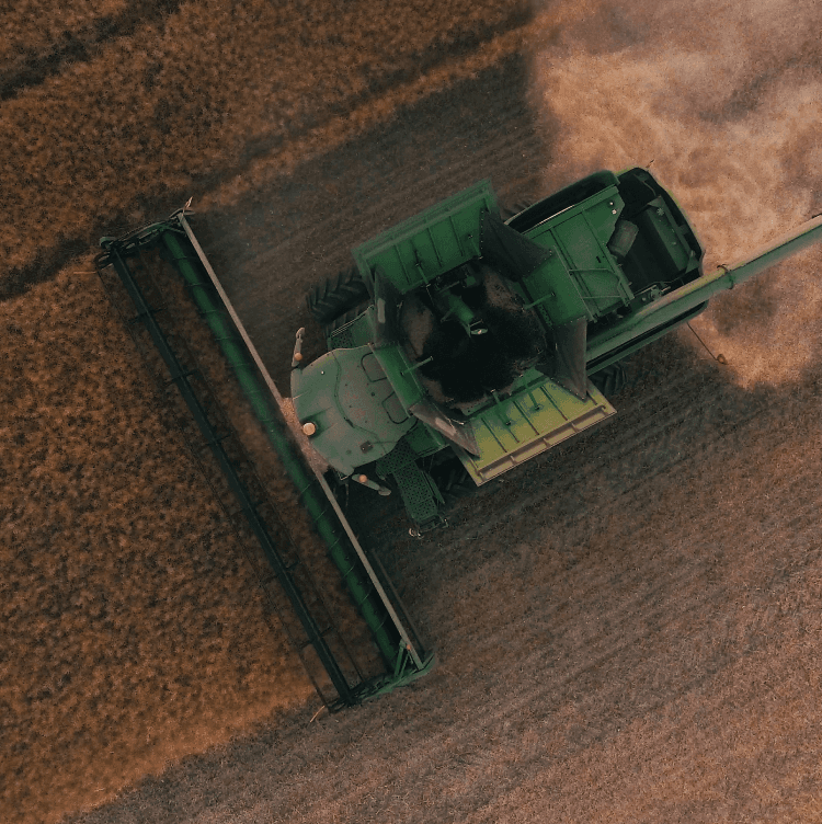 Aerial view of a green combine harvester cutting a field of golden crops
