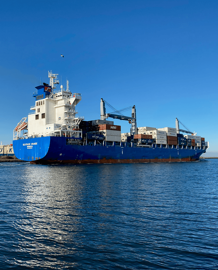 A container ship at sea leaving port, loaded with shipping containers.