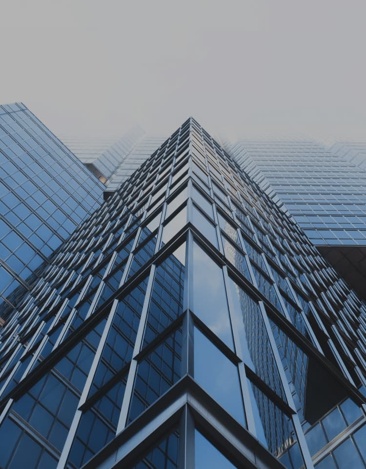 Looking up at a corner of a glass skyscraper rising into mist, with a blue tint