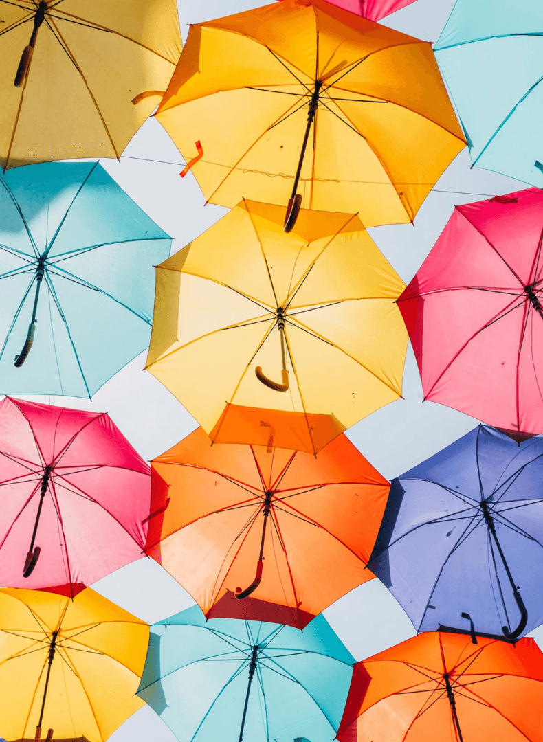 Colorful umbrellas in shades of yellow, blue, pink, orange, and purple, seen from below against a bright sky, forming a vibrant canopy.