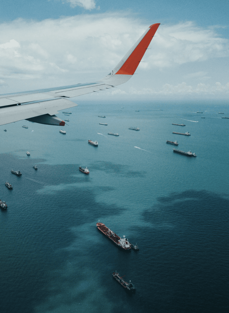 View from a plane window of the wing above blue sea dotted with cargo ships
