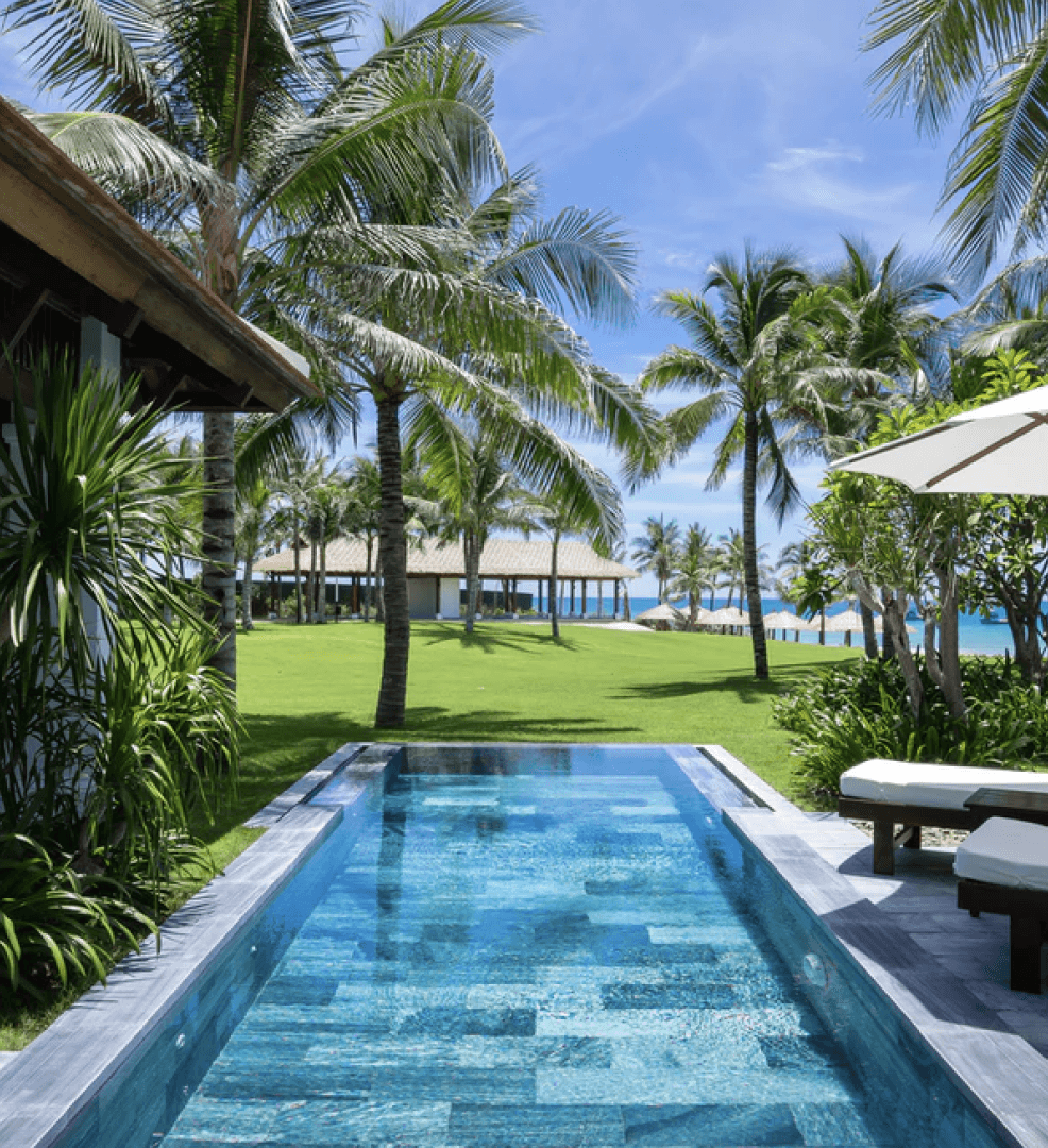 Villa swimming pool with a blue tiled floor, lawn and palm trees, with the sea in the distance